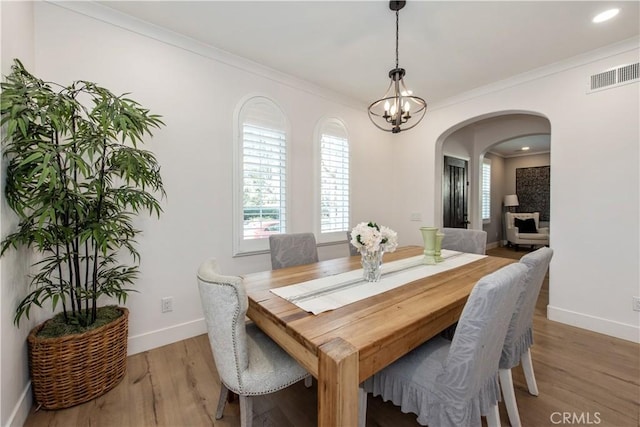 dining space featuring wood-type flooring, ornamental molding, and a chandelier