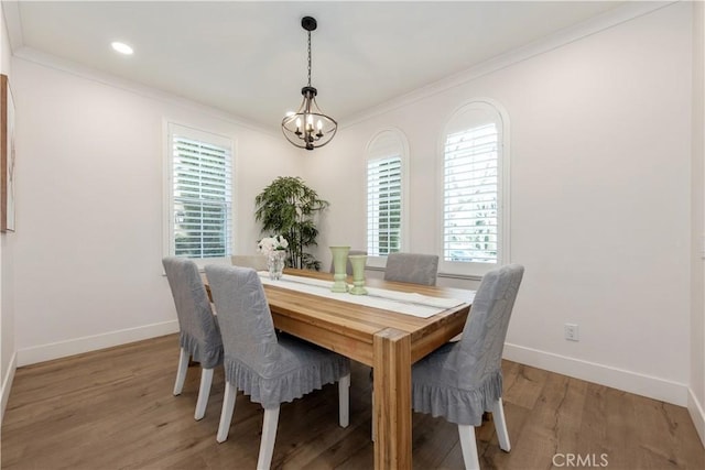 dining area with light wood-type flooring, ornamental molding, and a notable chandelier