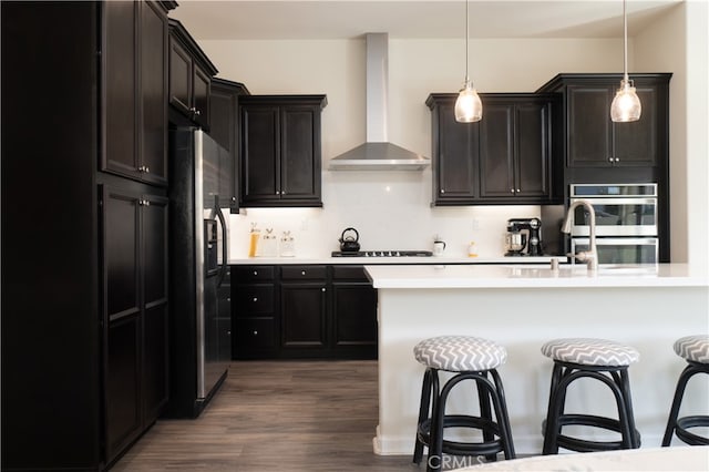 kitchen featuring backsplash, wall chimney range hood, hanging light fixtures, stainless steel appliances, and dark hardwood / wood-style flooring