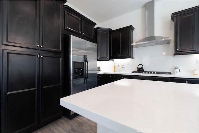 kitchen featuring stainless steel refrigerator with ice dispenser, gas cooktop, wall chimney range hood, and light hardwood / wood-style flooring