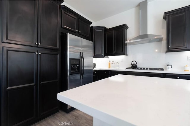 11121 Fourleaf Ct, Corona, CA 92883 - kitchen with wall chimney range hood, black stovetop, dark cabinetry, stainless steel fridge, and light countertops