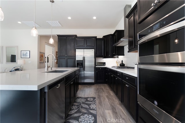 kitchen with pendant lighting, a center island with sink, sink, hardwood / wood-style flooring, and appliances with stainless steel finishes