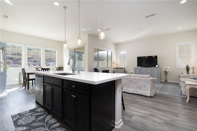 kitchen featuring dishwasher, light hardwood / wood-style floors, pendant lighting, sink, and an island with sink