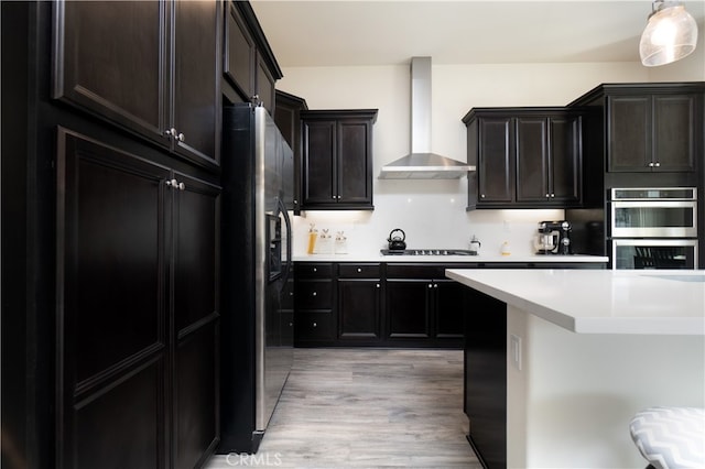 kitchen with pendant lighting, light hardwood / wood-style floors, decorative backsplash, stainless steel appliances, and wall chimney exhaust hood