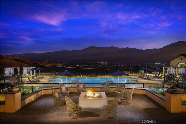 pool at dusk with a patio area, an outdoor fire pit, and a mountain view