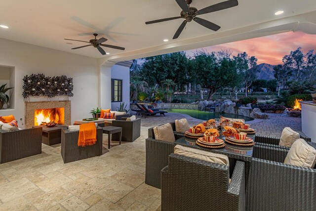 patio terrace at dusk featuring ceiling fan and an outdoor living space with a fireplace