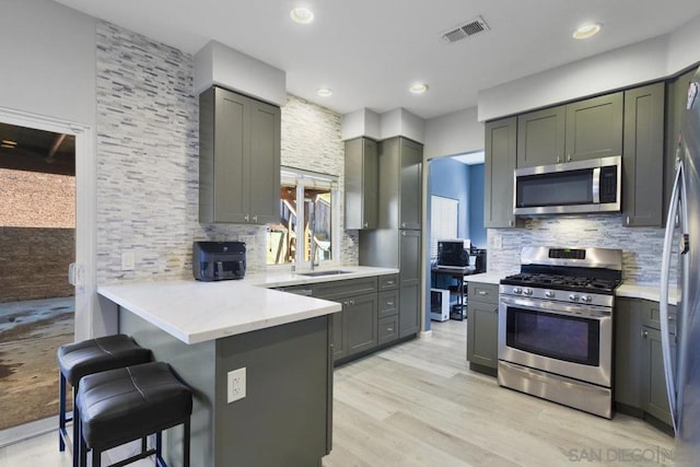 kitchen featuring a kitchen bar, kitchen peninsula, appliances with stainless steel finishes, decorative backsplash, and sink