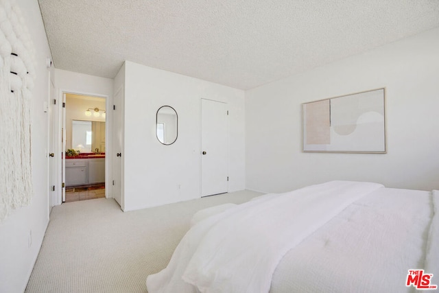 bedroom with ensuite bath, light carpet, and a textured ceiling