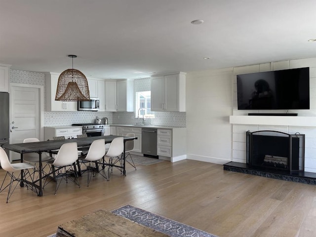 dining space with light wood-type flooring, a tiled fireplace, and sink