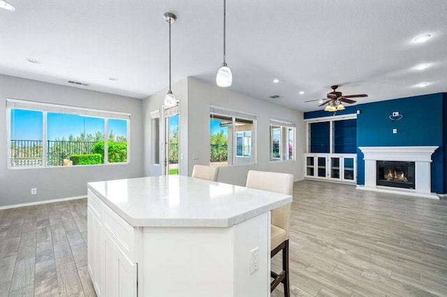 kitchen with white cabinets, light hardwood / wood-style floors, a kitchen breakfast bar, hanging light fixtures, and ceiling fan