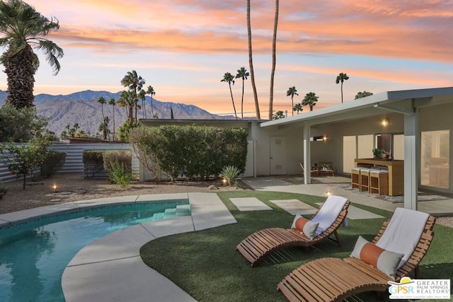 pool at dusk with exterior bar, a patio area, and a mountain view