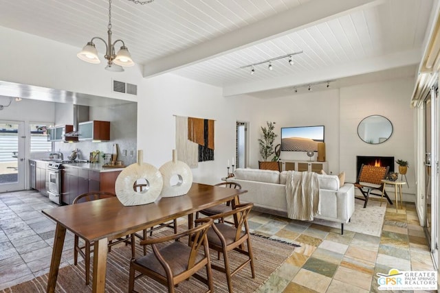 dining space featuring beam ceiling, a large fireplace, sink, track lighting, and a chandelier