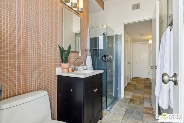 bathroom with toilet, tile walls, a shower with shower door, and vanity