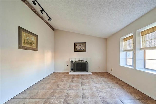 unfurnished living room with a textured ceiling, track lighting, a fireplace, vaulted ceiling, and light tile patterned floors