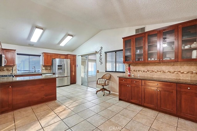 kitchen featuring appliances with stainless steel finishes, vaulted ceiling, tasteful backsplash, stone countertops, and light tile patterned flooring