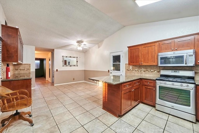 kitchen featuring appliances with stainless steel finishes, lofted ceiling, kitchen peninsula, and dark stone counters