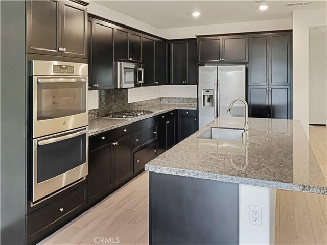 kitchen featuring light stone counters, sink, stainless steel appliances, and a center island with sink