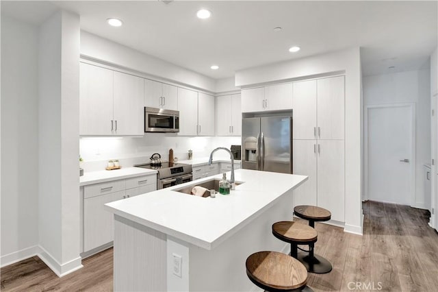 kitchen with white cabinets, appliances with stainless steel finishes, an island with sink, and sink