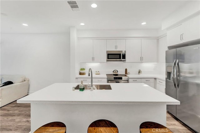 kitchen featuring an island with sink, light wood-type flooring, white cabinetry, appliances with stainless steel finishes, and sink