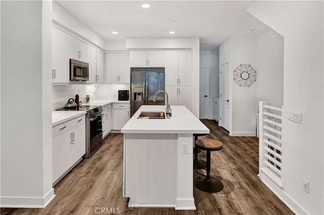 kitchen featuring hardwood / wood-style floors, a kitchen island with sink, appliances with stainless steel finishes, white cabinets, and sink