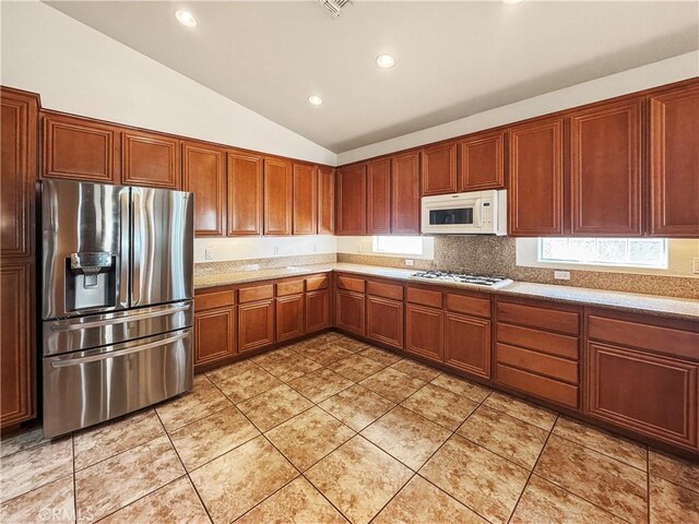 kitchen with tasteful backsplash, stainless steel fridge with ice dispenser, light tile patterned floors, and vaulted ceiling