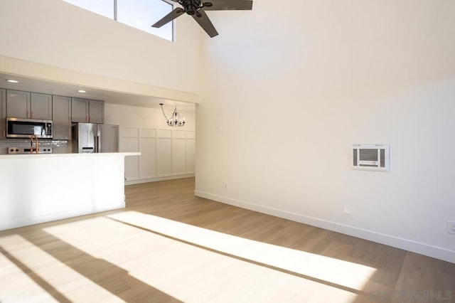 unfurnished living room featuring light wood-type flooring, a towering ceiling, and ceiling fan with notable chandelier