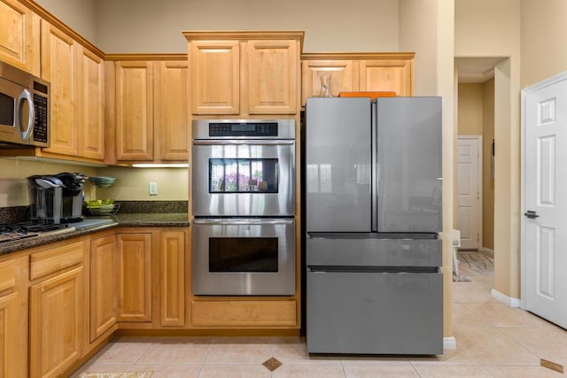 kitchen with dark stone countertops, appliances with stainless steel finishes, and light tile patterned flooring