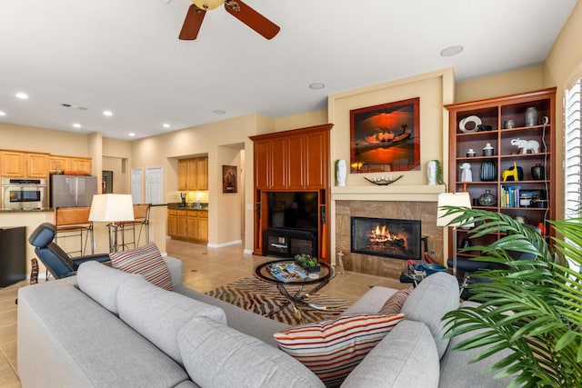 living room with ceiling fan, a tiled fireplace, and light tile patterned flooring