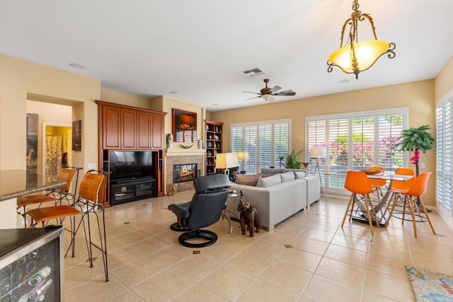 living room with ceiling fan, a tiled fireplace, and light tile patterned flooring