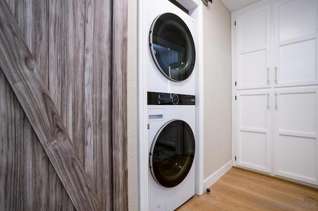 laundry room with light hardwood / wood-style floors, stacked washer / dryer, and a barn door