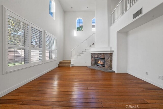 unfurnished living room with a fireplace, wood-type flooring, and a towering ceiling