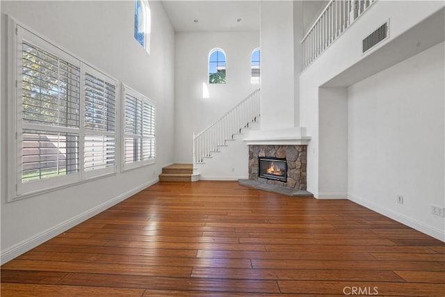 unfurnished living room with hardwood / wood-style flooring, a stone fireplace, a healthy amount of sunlight, and a high ceiling