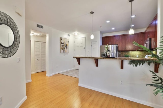 kitchen featuring a breakfast bar, light wood-type flooring, stainless steel fridge, pendant lighting, and backsplash