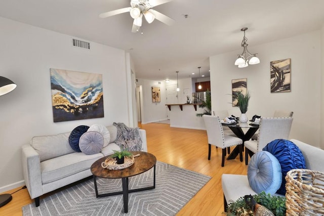 living room with ceiling fan with notable chandelier and light hardwood / wood-style flooring