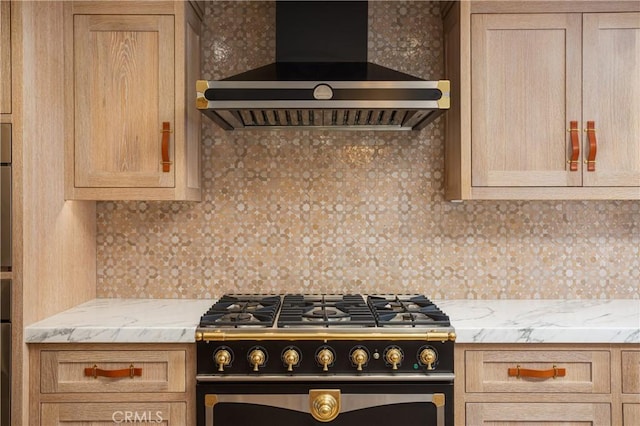 kitchen with light stone countertops, wall chimney exhaust hood, gas stove, light brown cabinetry, and backsplash