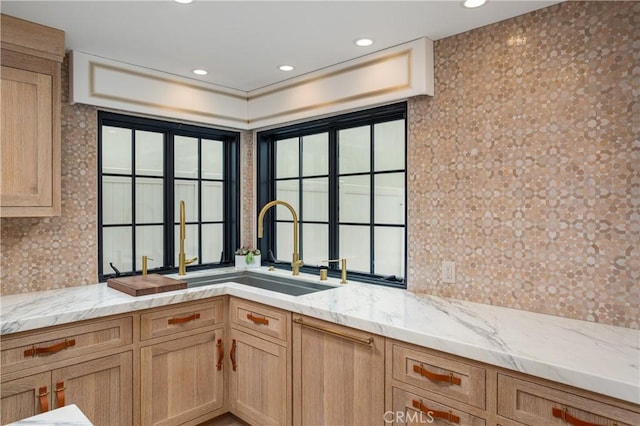 kitchen with light brown cabinetry, sink, and light stone counters