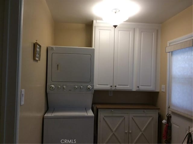 laundry area with stacked washer / dryer and cabinets