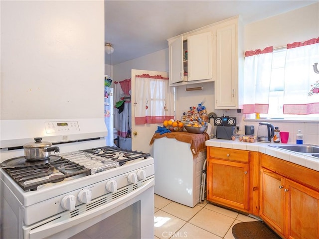 kitchen with light tile patterned floors, gas range gas stove, white cabinetry, tile counters, and sink