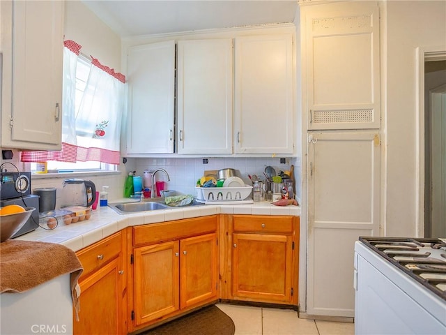 kitchen with backsplash, tile countertops, sink, light tile patterned floors, and white cabinets