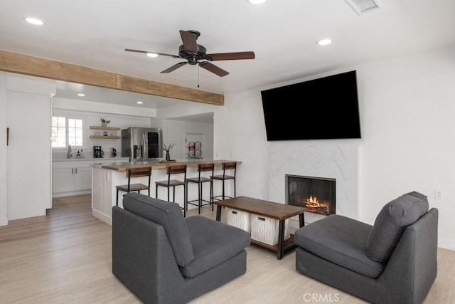 living room with ceiling fan, beamed ceiling, light hardwood / wood-style floors, and a premium fireplace