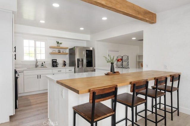 kitchen with white cabinets, a kitchen bar, stainless steel refrigerator with ice dispenser, beamed ceiling, and sink