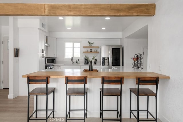 kitchen with kitchen peninsula, stainless steel appliances, a kitchen bar, and white cabinetry