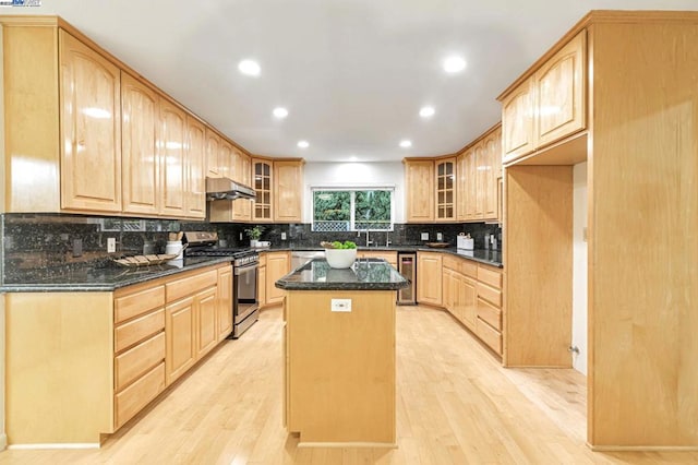 kitchen featuring light hardwood / wood-style flooring, stainless steel appliances, a center island, wine cooler, and dark stone counters