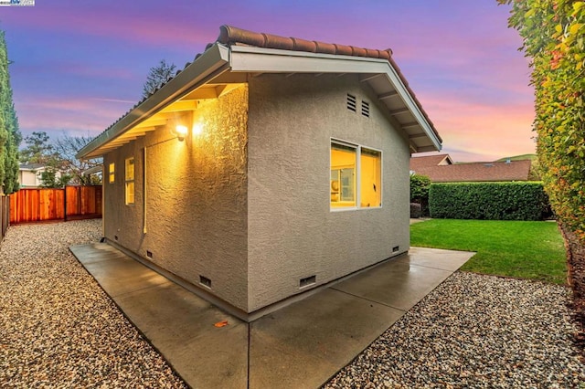 property exterior at dusk featuring a patio area and a lawn