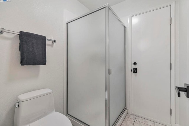 bathroom featuring tile patterned flooring, a shower with door, and toilet