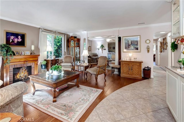 living room with a brick fireplace, crown molding, ceiling fan, and light wood-type flooring