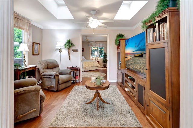 living room with ceiling fan, a skylight, crown molding, and light hardwood / wood-style floors