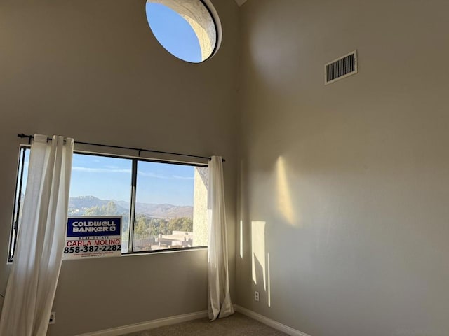 unfurnished room with carpet, a mountain view, and a towering ceiling