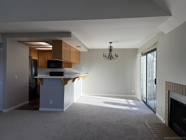 kitchen with black appliances, an inviting chandelier, a fireplace, kitchen peninsula, and a breakfast bar area