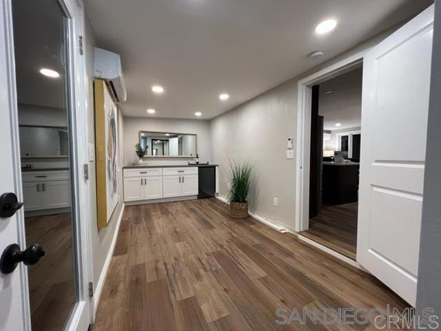 kitchen with wood-type flooring, white cabinets, and a wall mounted air conditioner